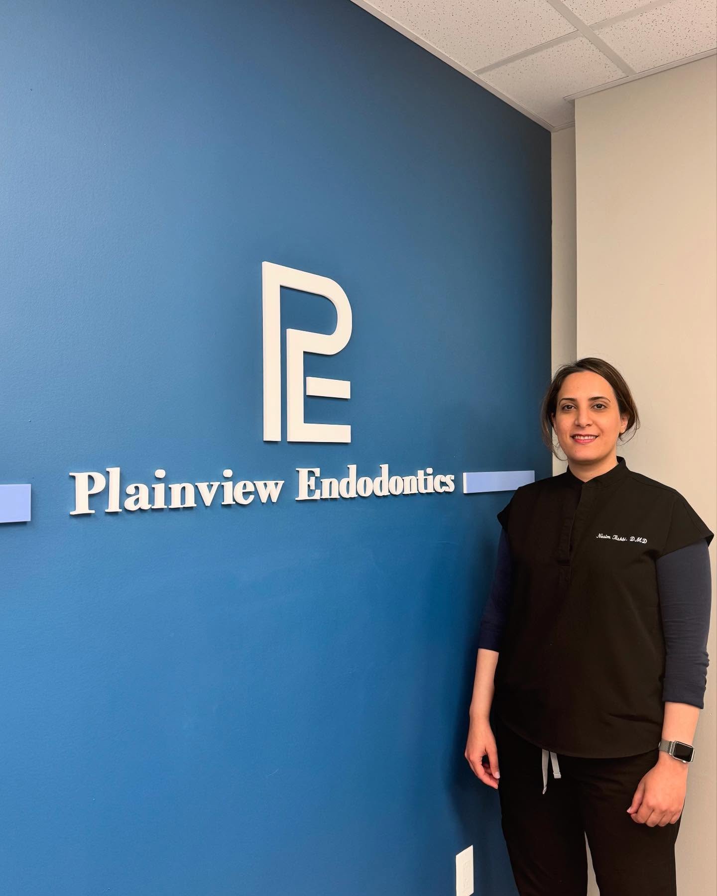 Dr. Nasim Tishbi standing beside the Plainview Endodontics wall sign
